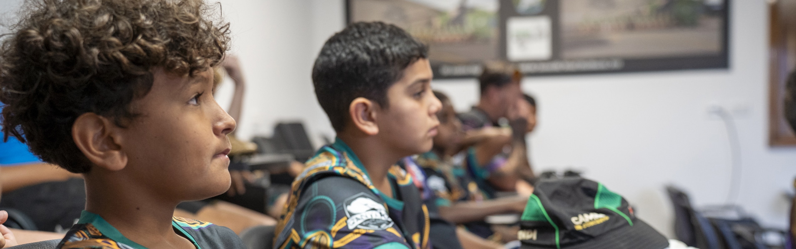 Side profile of a boy with curly hair wearing a colorful jersey, attentively listening in a classroom.